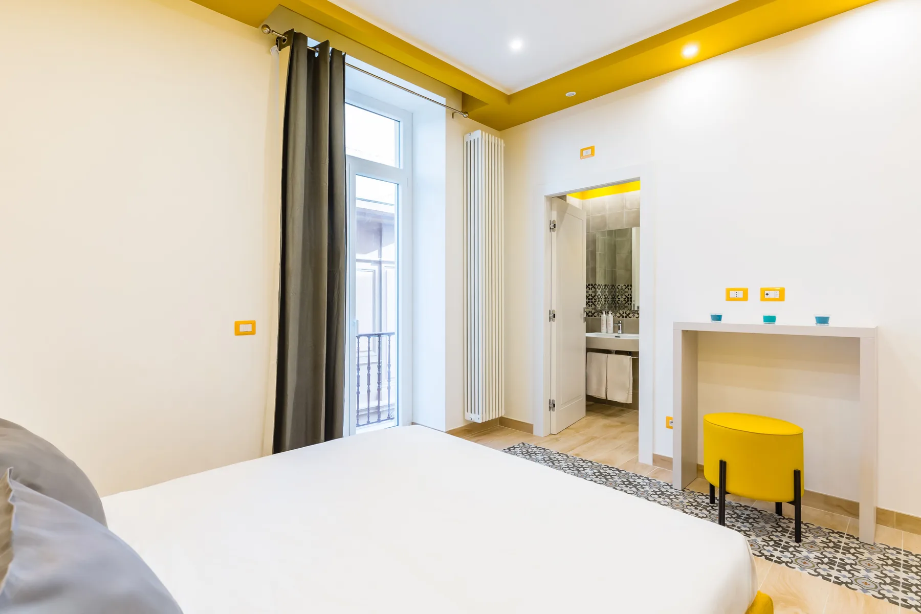 A bedroom with a bed beside a tall window and a small desk.