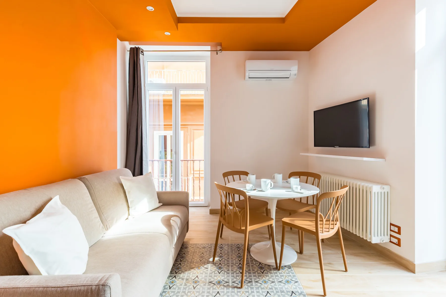 A bright living and dining room with a sofa, table, and wall-mounted television.