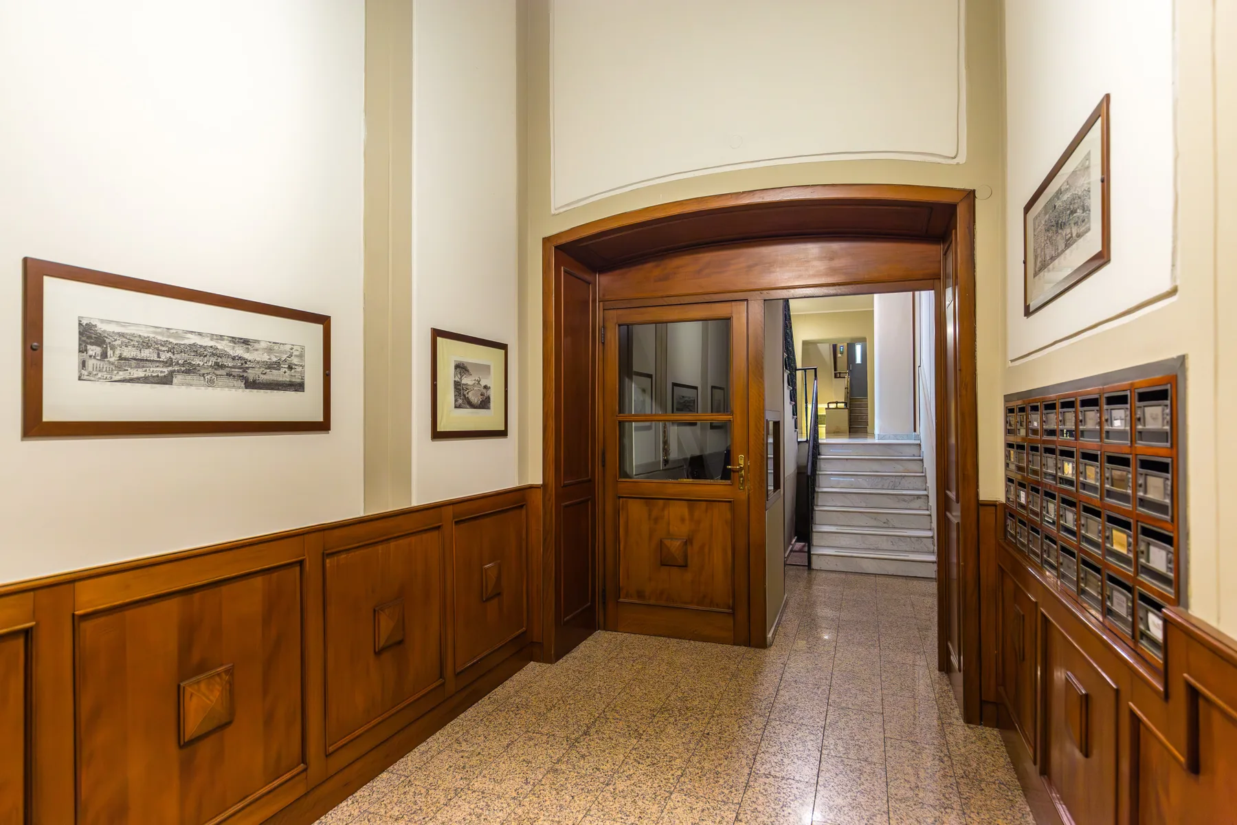 An interior hallway with wood paneling, framed artwork, and stairs at the far end.