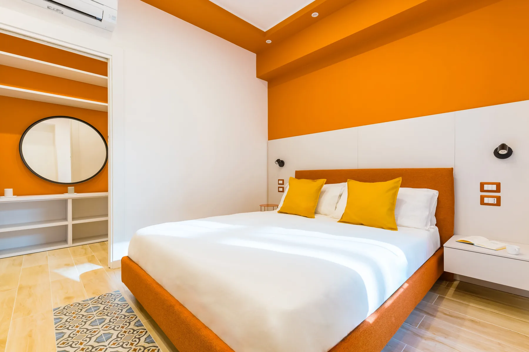 A bedroom with a bed dressed in white and bright orange accents.