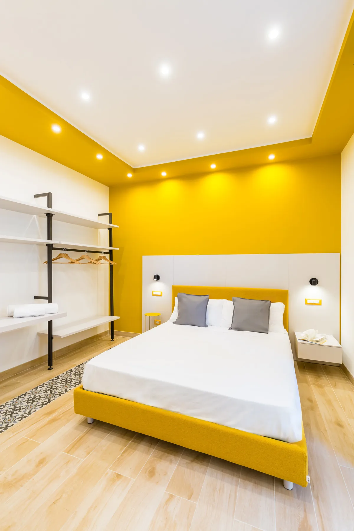 A bedroom with a bed against a bright yellow accent wall.