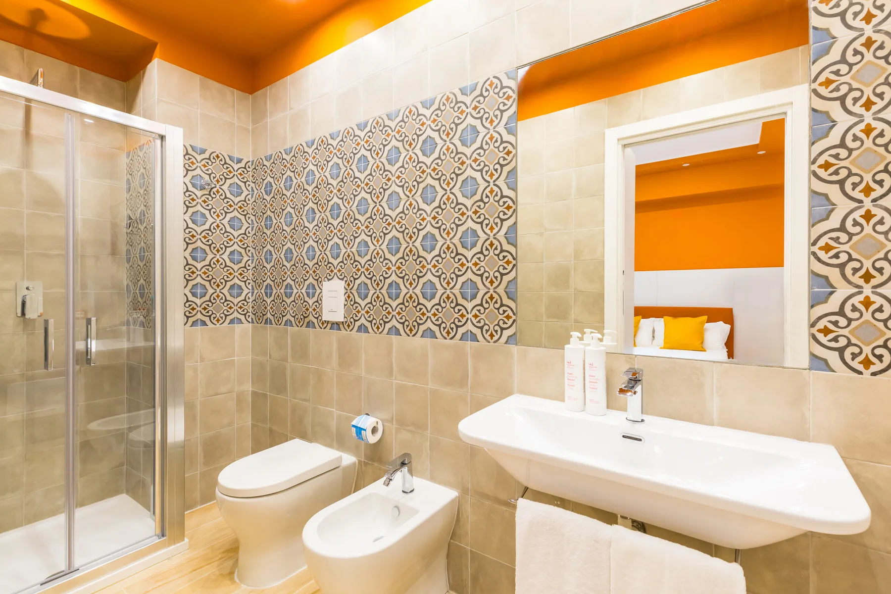 A bathroom with a glass shower, sink, and patterned tile accents.