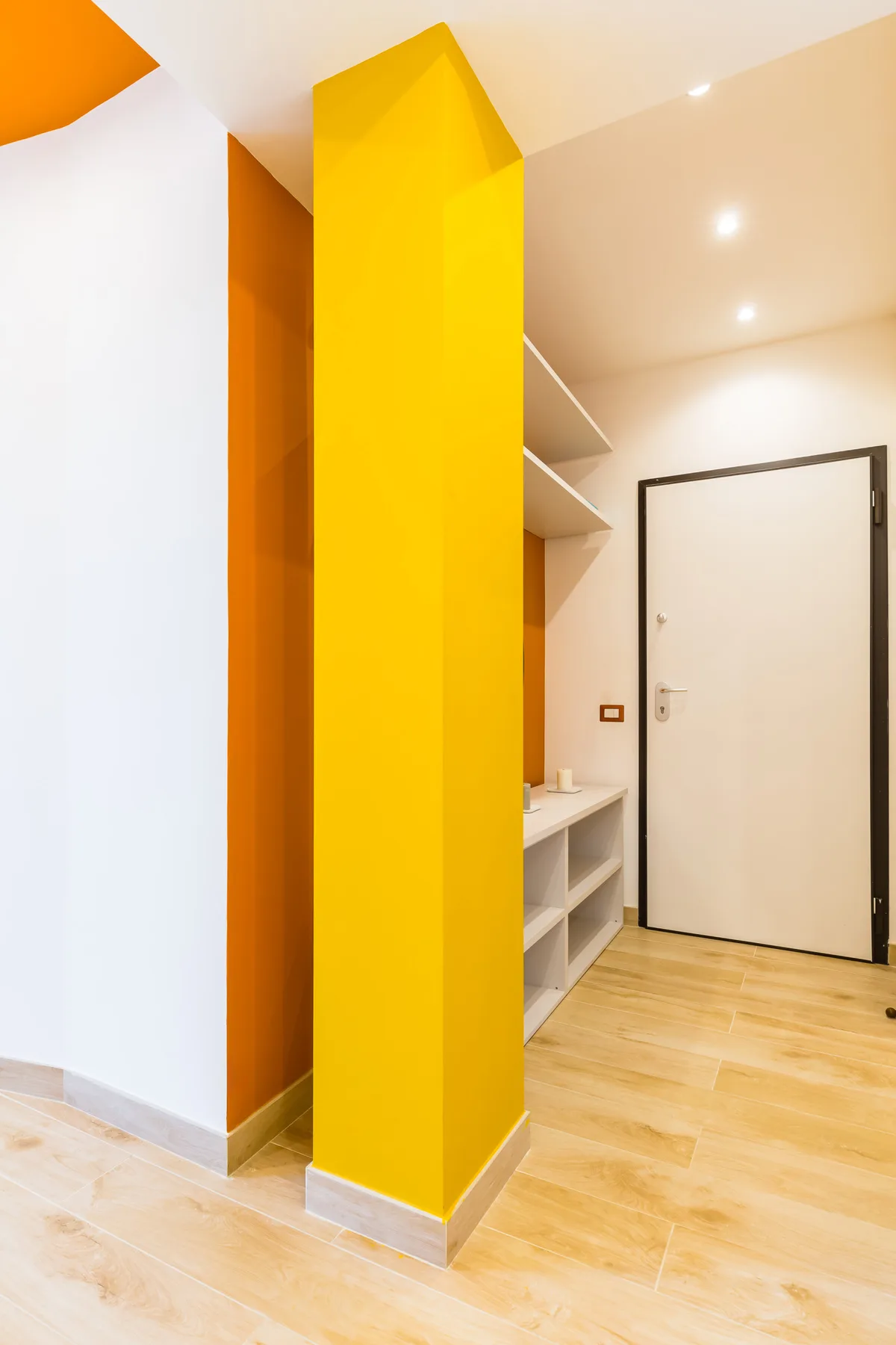 A bright entryway with a white door, open shelving, and a yellow partition.