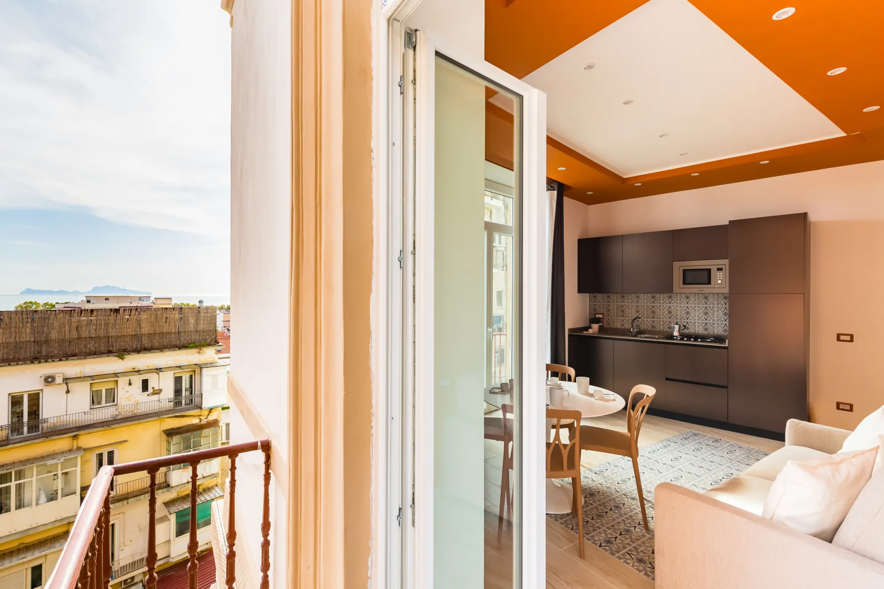 A bright dining and living area opens onto a balcony, with a kitchen along the back wall.
