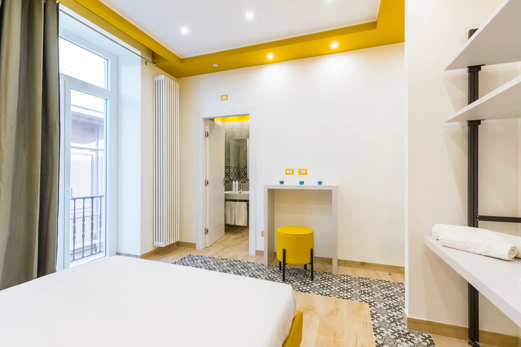A bright bedroom with a bed, tall window, and doorway to the bathroom.