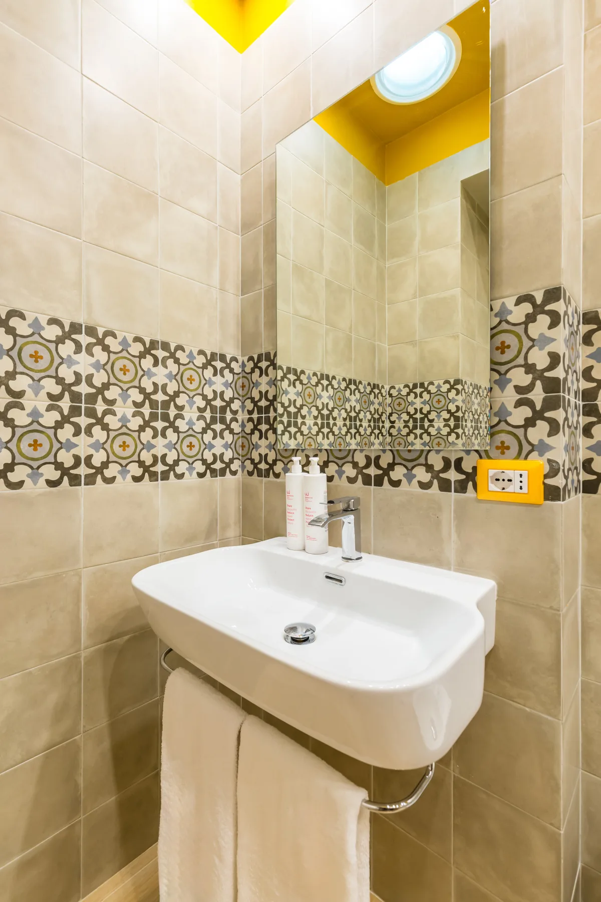 A tiled bathroom vanity with a wall-mounted sink and mirror.
