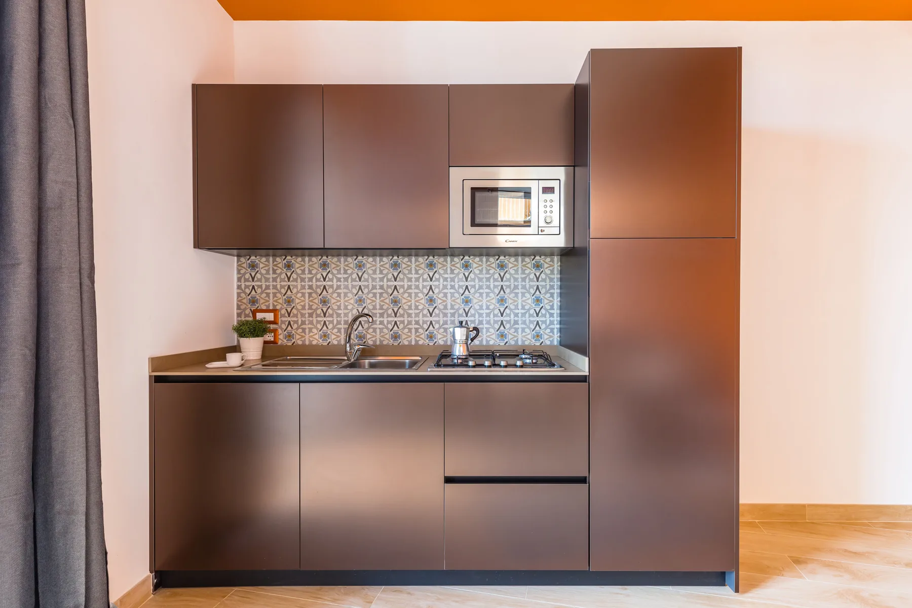 A compact kitchen with dark cabinets, a patterned backsplash, and a countertop.
