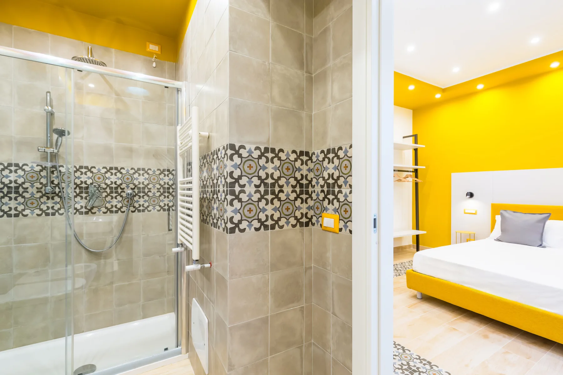 A tiled bathroom with a glass shower beside a bedroom with bright yellow walls.