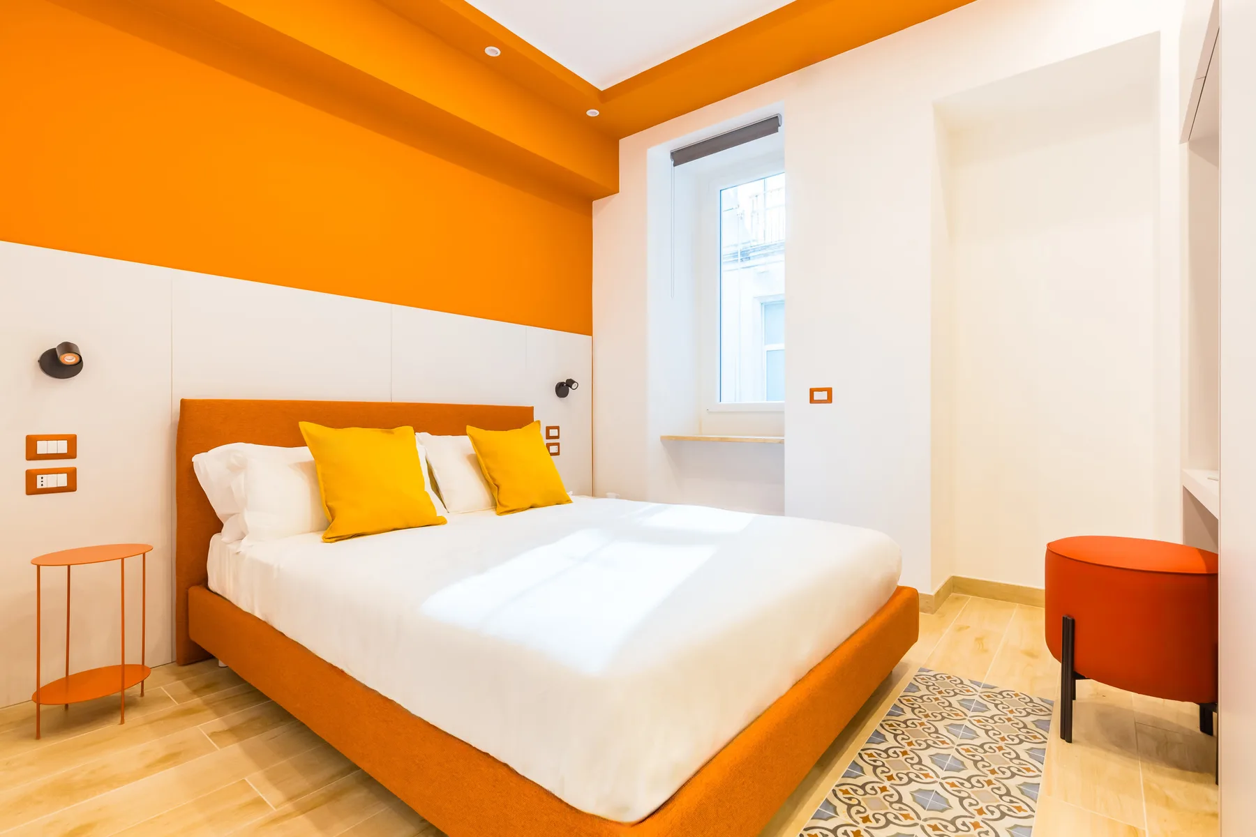 A bedroom with a large bed, white bedding, and bright orange accents.