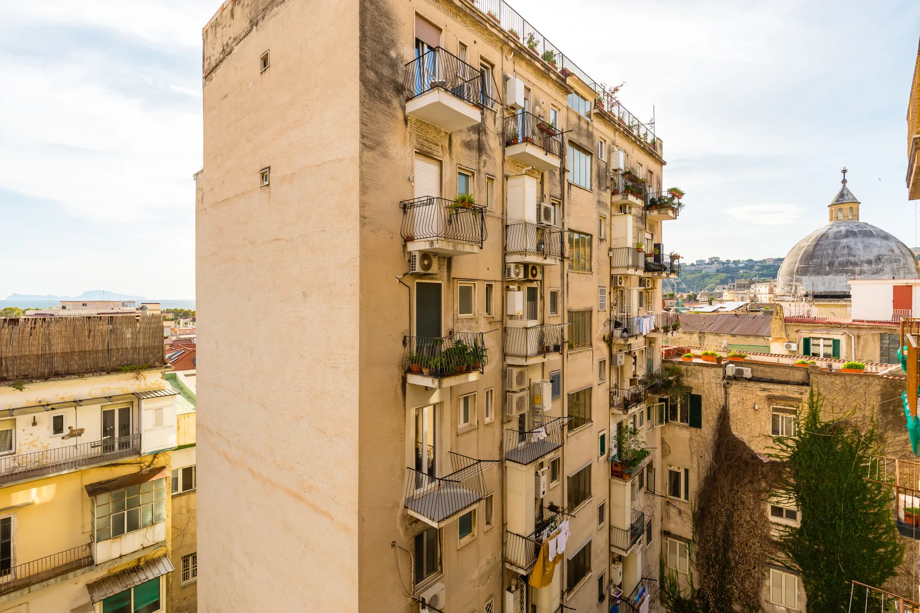 A view of a tan apartment building with balconies and a domed structure nearby.