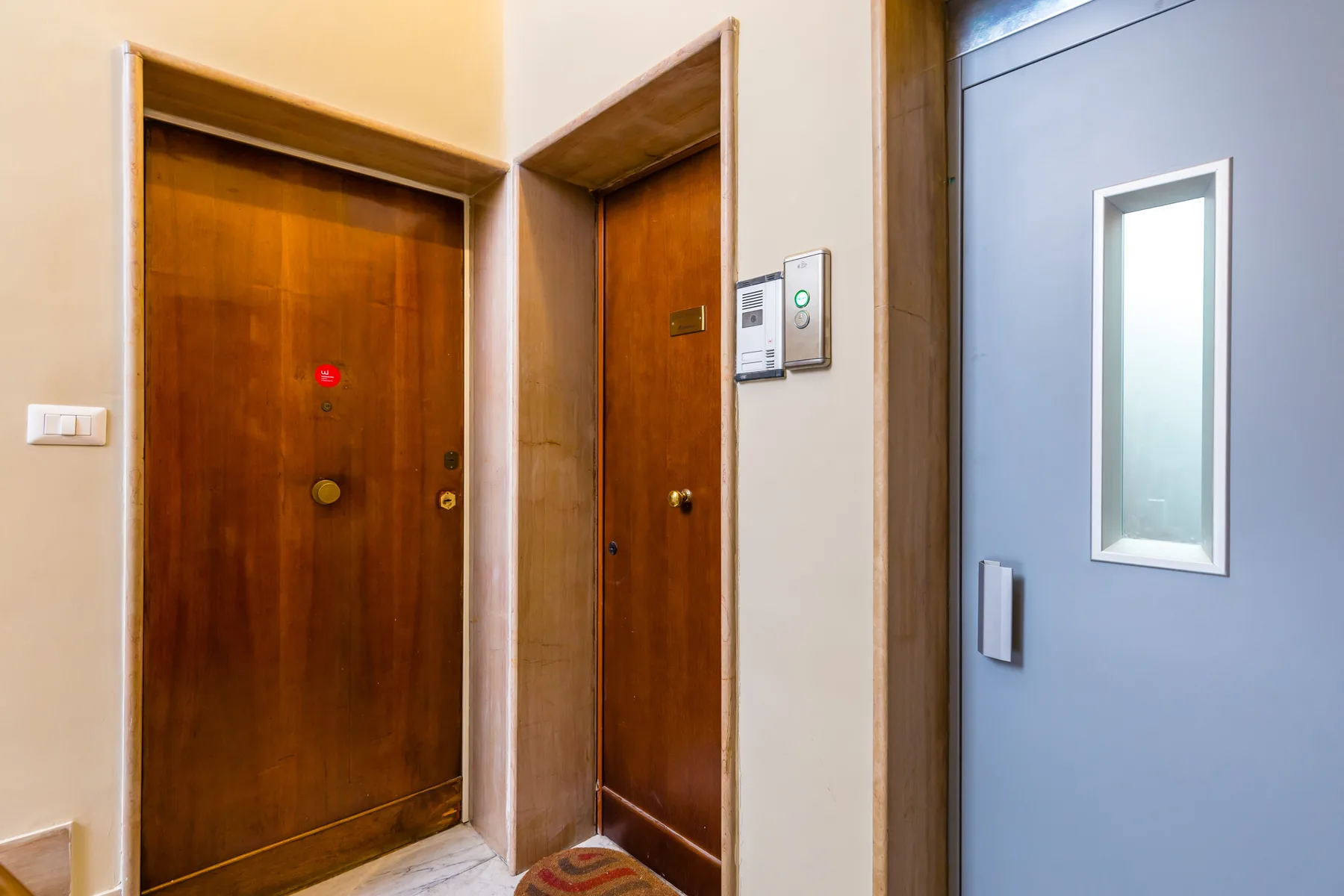 An indoor hallway with wooden doors and a gray door with a window.