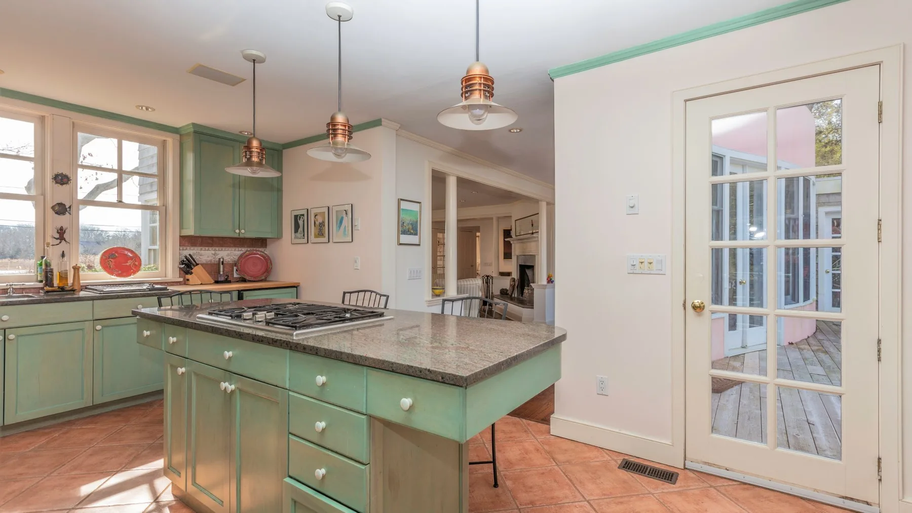 Una cocina luminosa con gabinetes verdes, una isla central y ventanas grandes.