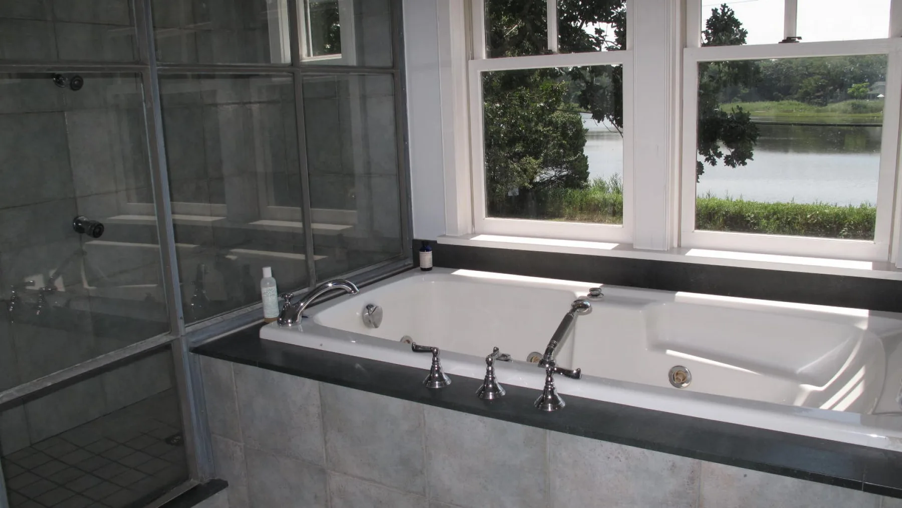 Un baño con bañera junto a una ducha de vidrio y grandes ventanas con vista al agua.
