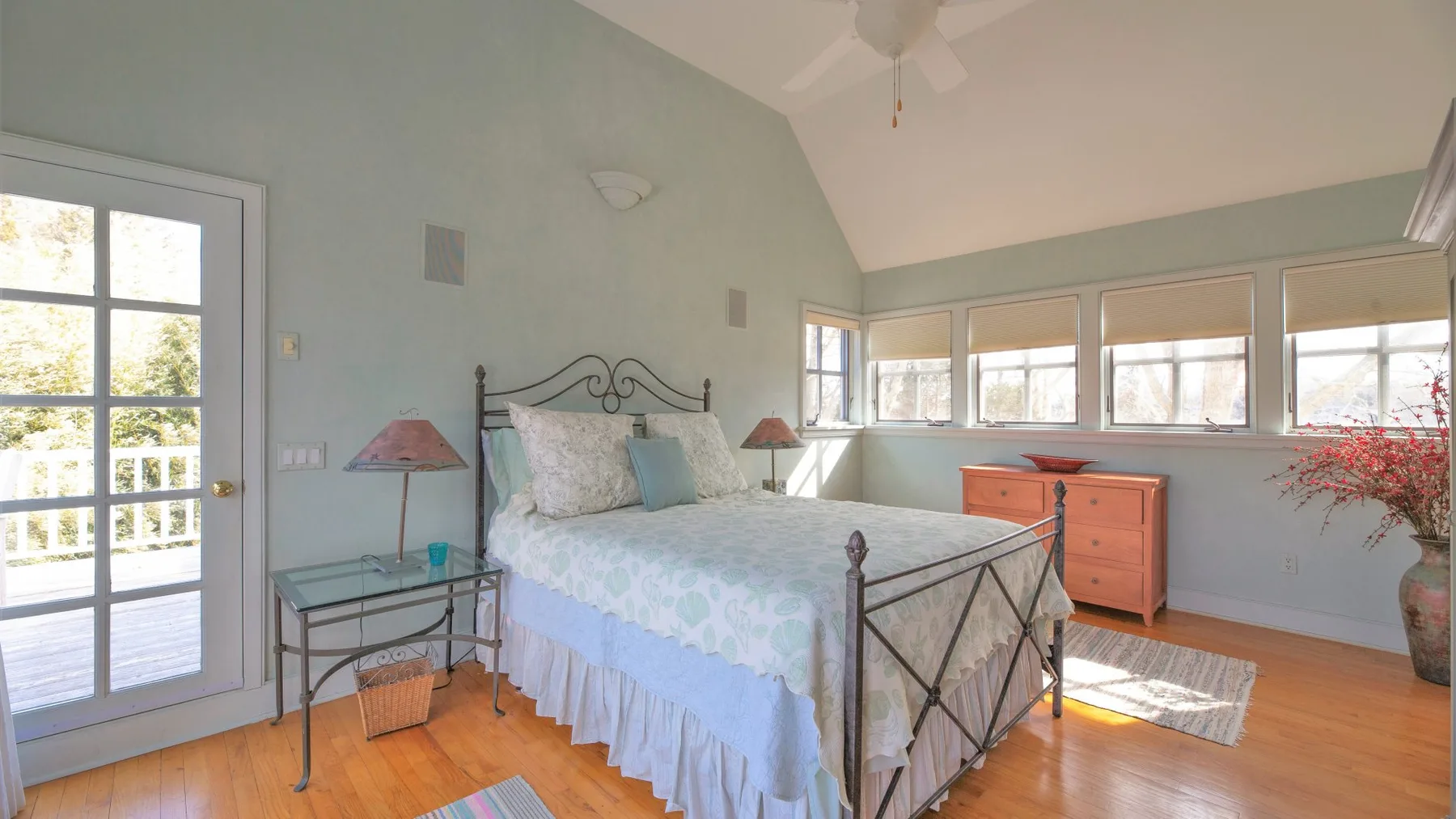 Un dormitorio luminoso con una cama, una mesita de noche y ventanas en la pared del fondo.