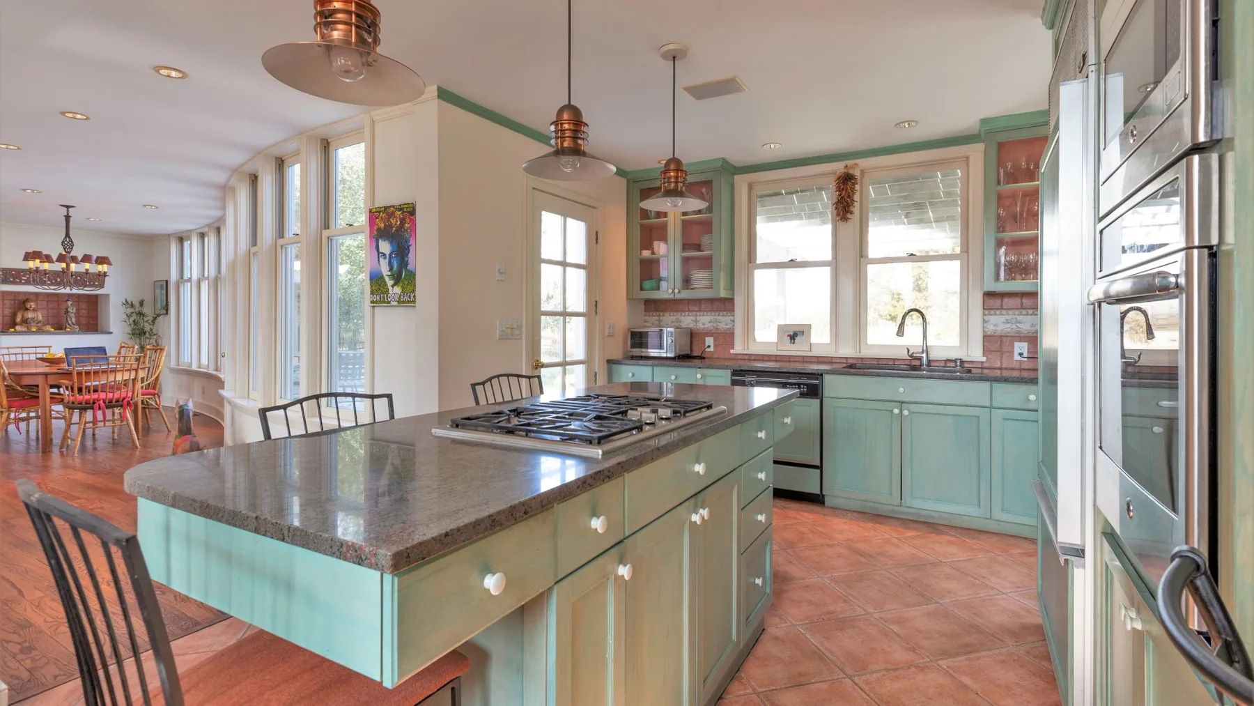 Una cocina amplia con isla central, gabinetes verdes y ventanas grandes.