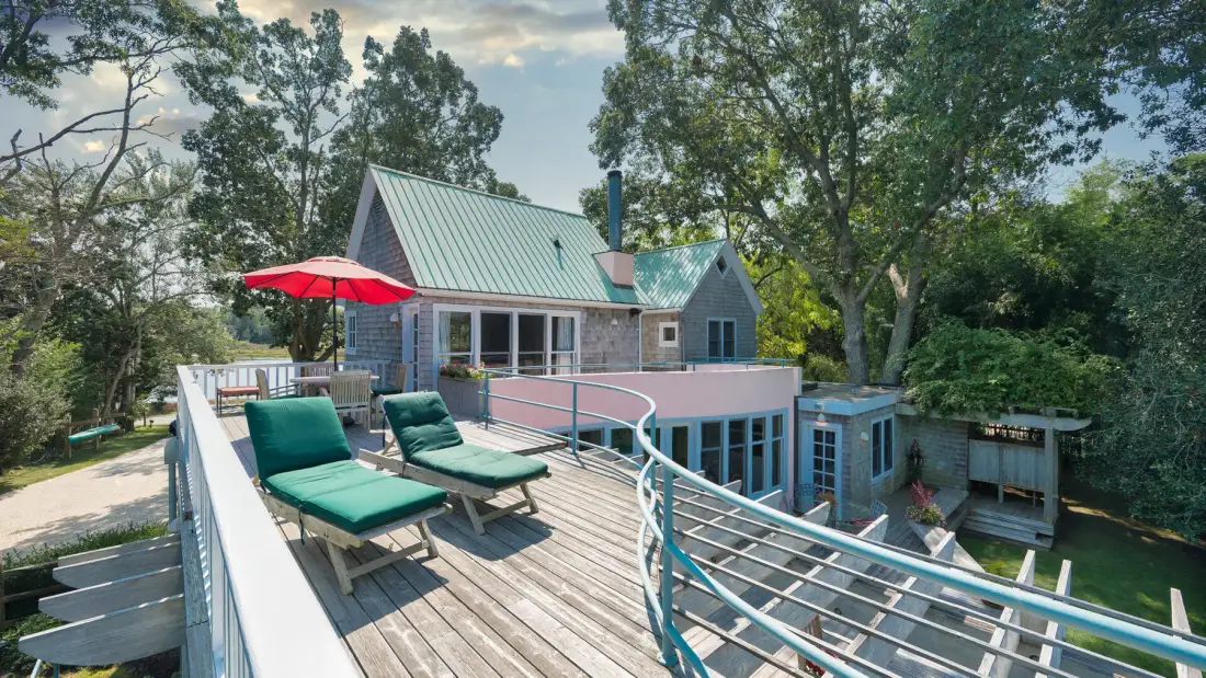 Una terraza exterior con asientos acolchados mira hacia una casa y árboles.