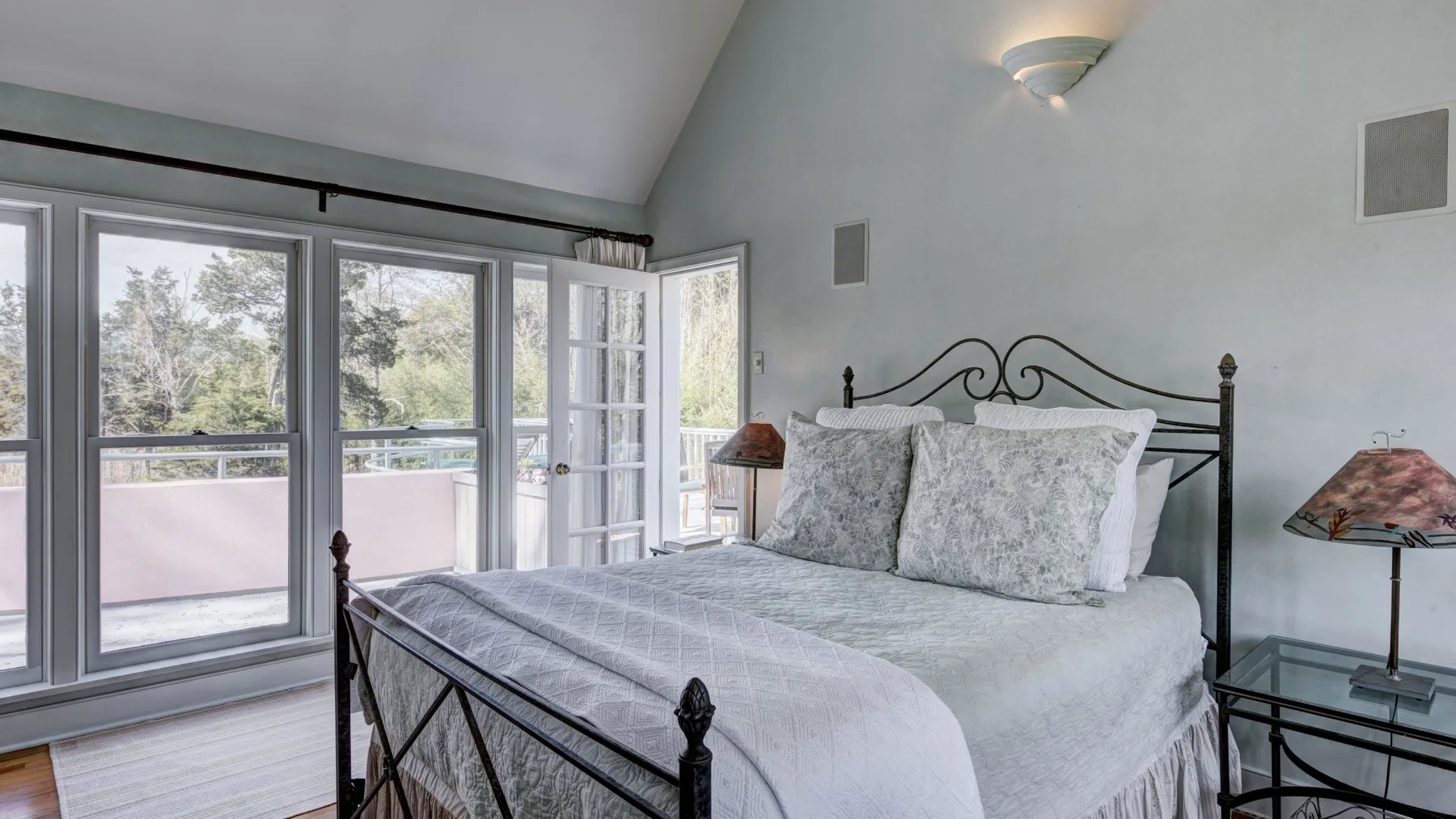 Un dormitorio luminoso con una cama bien tendida junto a grandes ventanas.