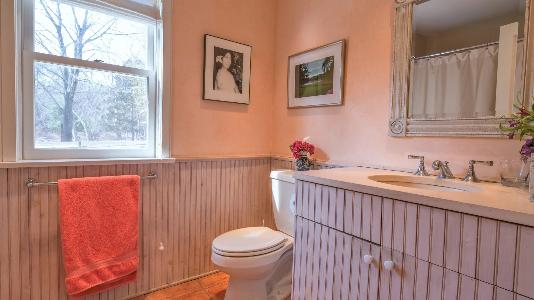 Un baño con inodoro, lavabo y una toalla naranja junto a la ventana.