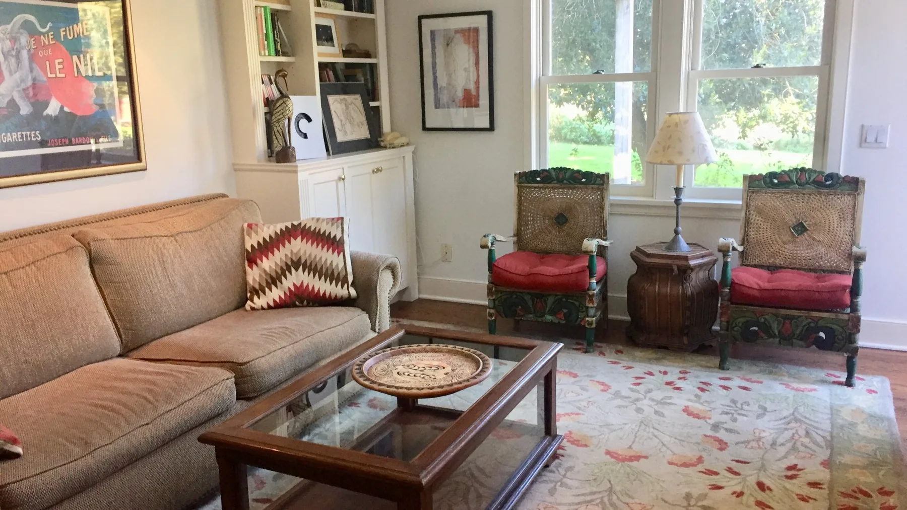 Una sala de estar con un sofá, una mesa de centro con tapa de vidrio y asientos junto a las ventanas.