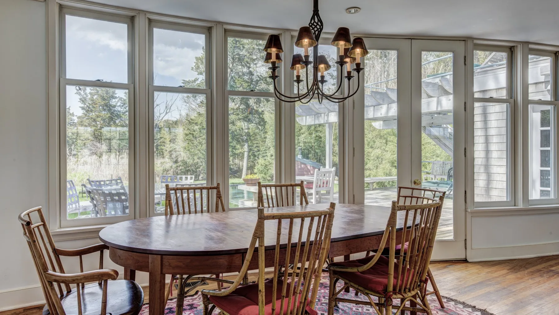Un comedor con una mesa de madera y sillas junto a grandes ventanas.