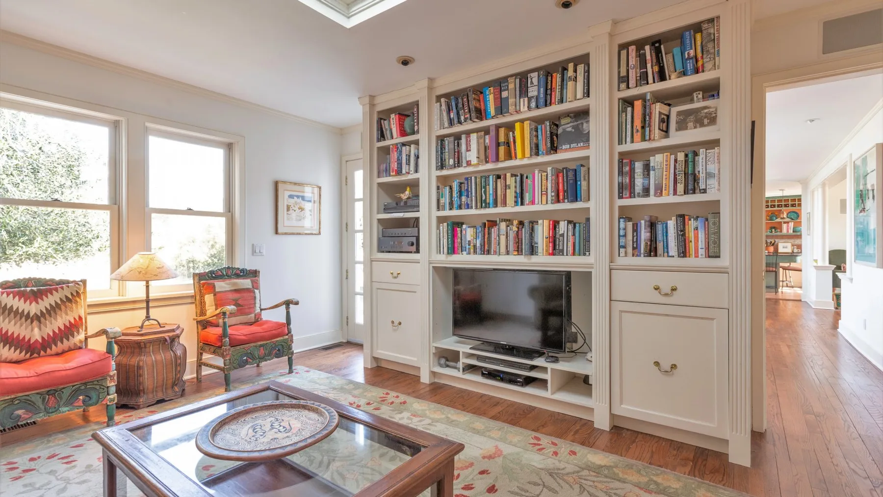 Una sala de estar luminosa con estanterías empotradas, un televisor y asientos junto a las ventanas.
