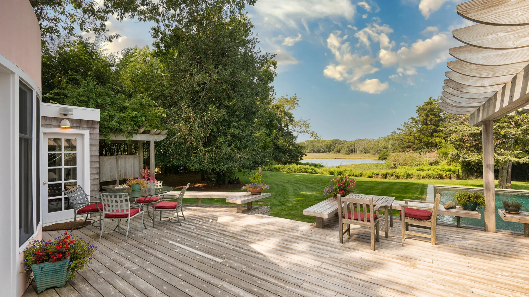 Un patio al aire libre con asientos para comer y descansar da a un paisaje verde y al agua.
