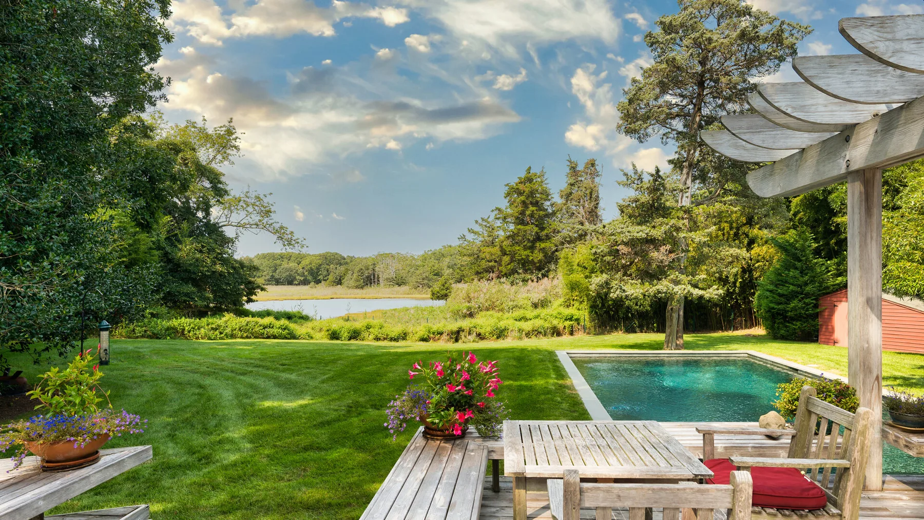 Un jardín ajardinado rodea una piscina, con árboles y una pérgola de madera.