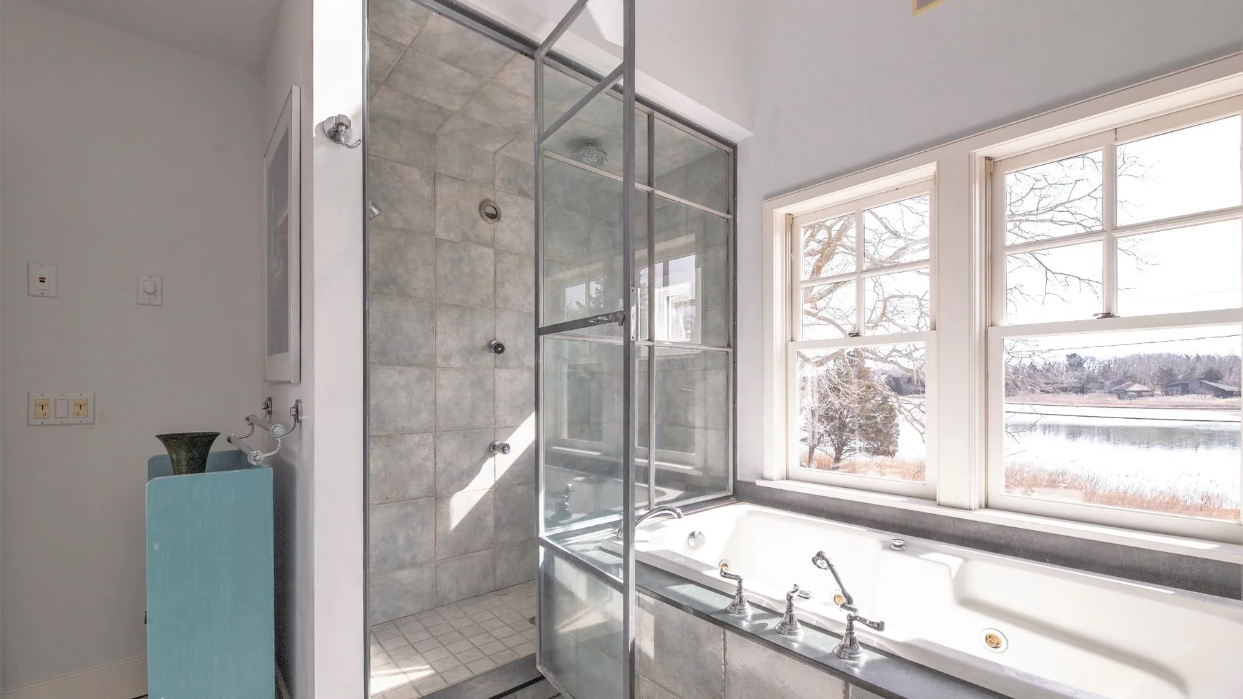 Un baño con ducha de vidrio, bañera y grandes ventanas con vistas al exterior.