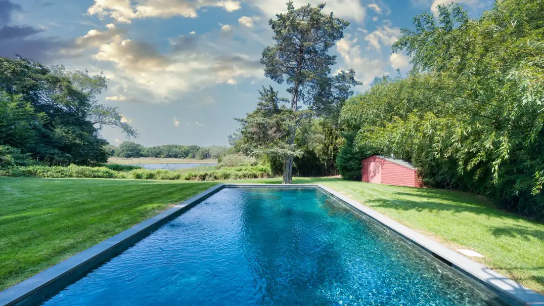 Una piscina al aire libre está junto a un césped y árboles.