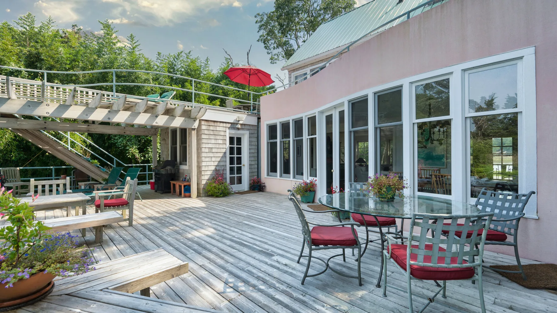 Una terraza exterior con asientos junto a un edificio rosa y ventanas grandes.