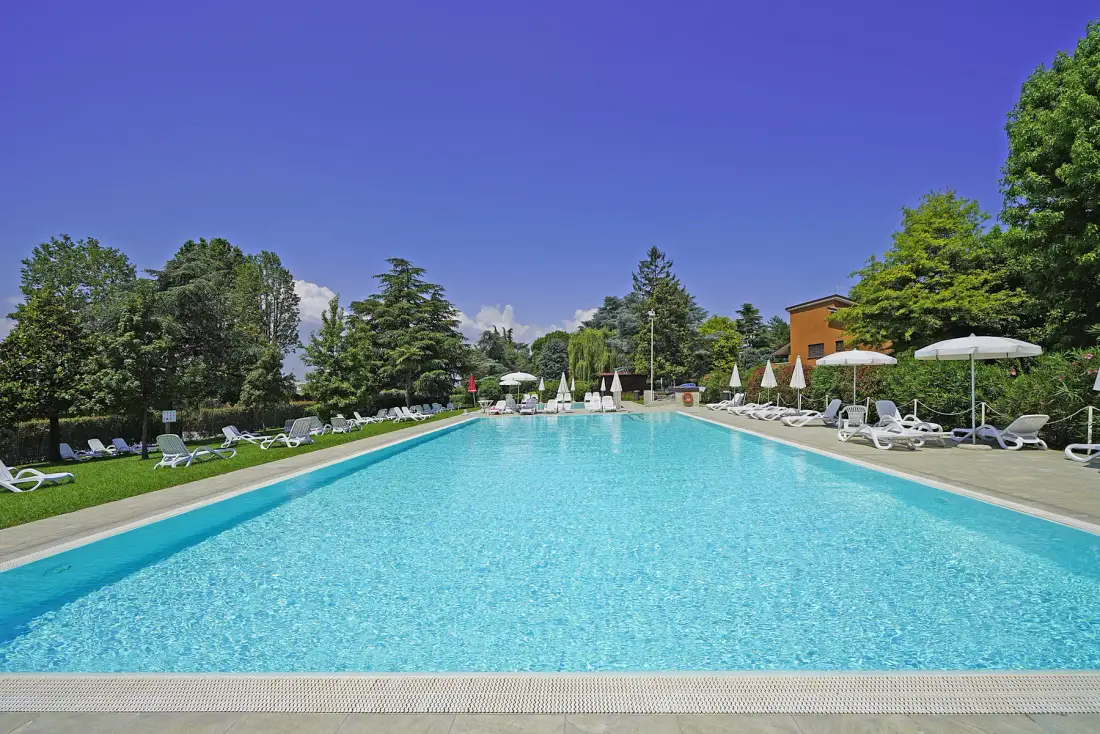 Una piscina al aire libre está rodeada de árboles y asientos para descansar.