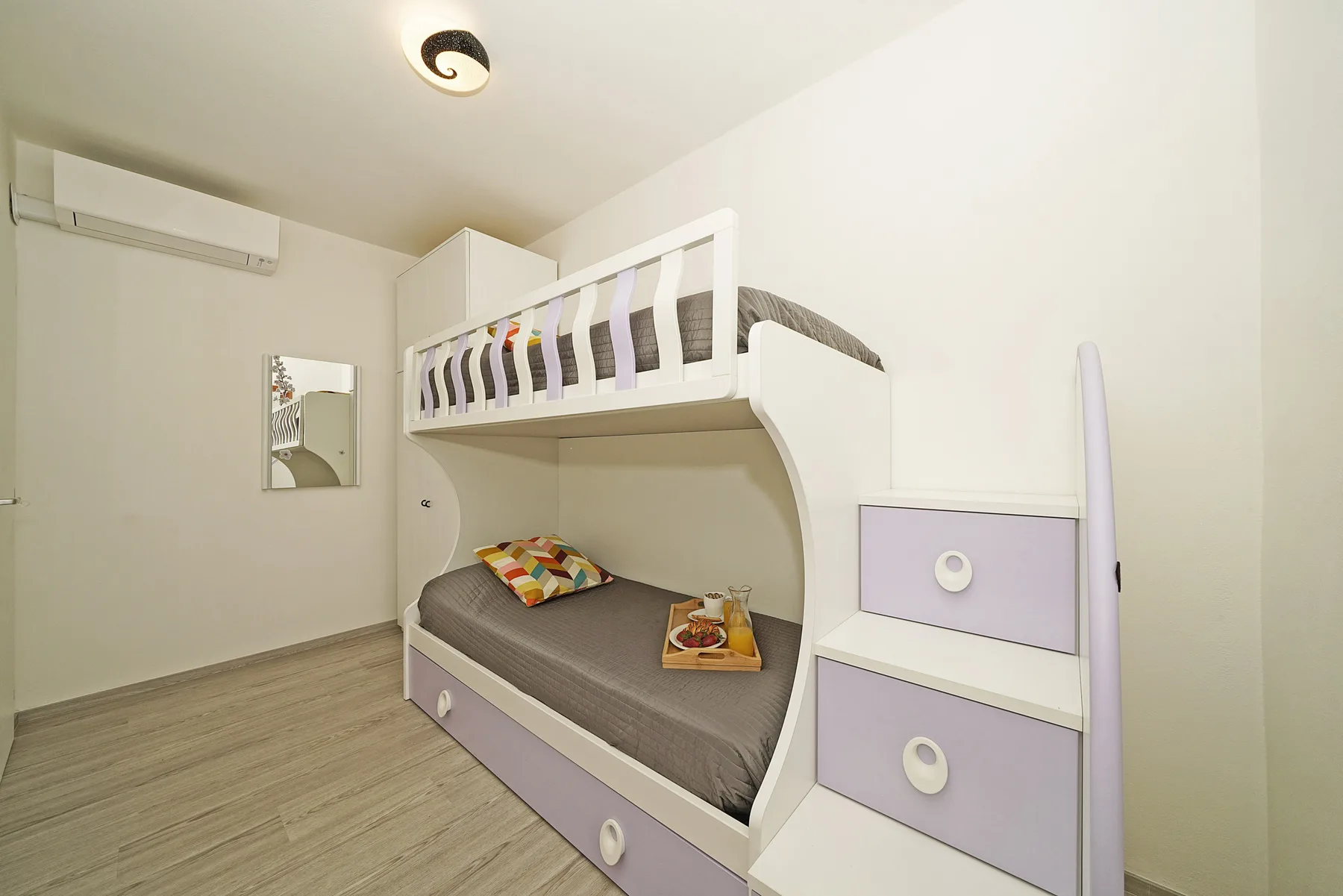 Un dormitorio compacto tiene una cama elevada sobre otra cama con ropa de cama gris.