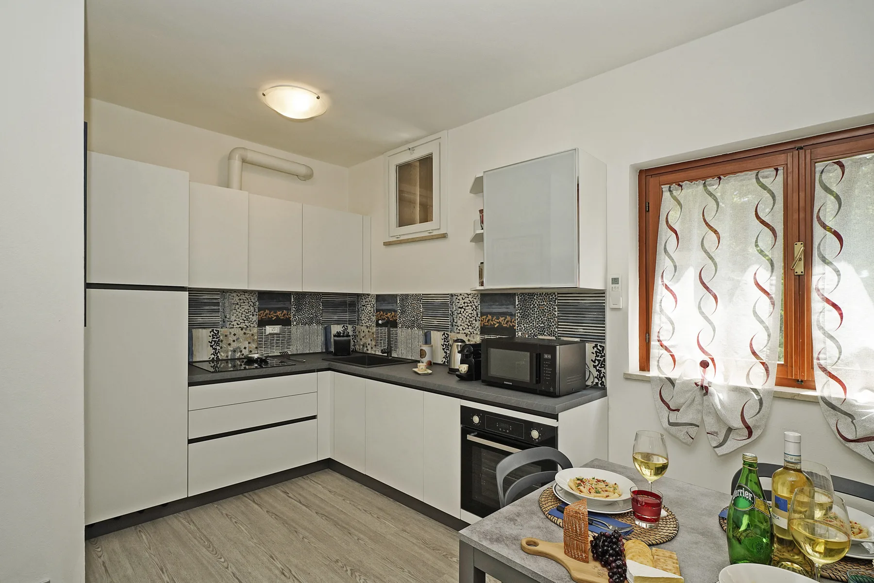 Una cocina compacta con gabinetes blancos, una encimera oscura y una mesa de comedor.