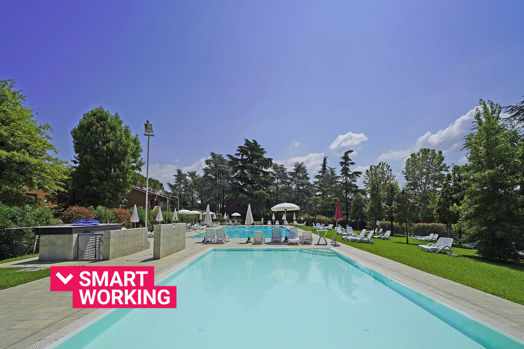 Una piscina al aire libre está rodeada de asientos reclinables y árboles.