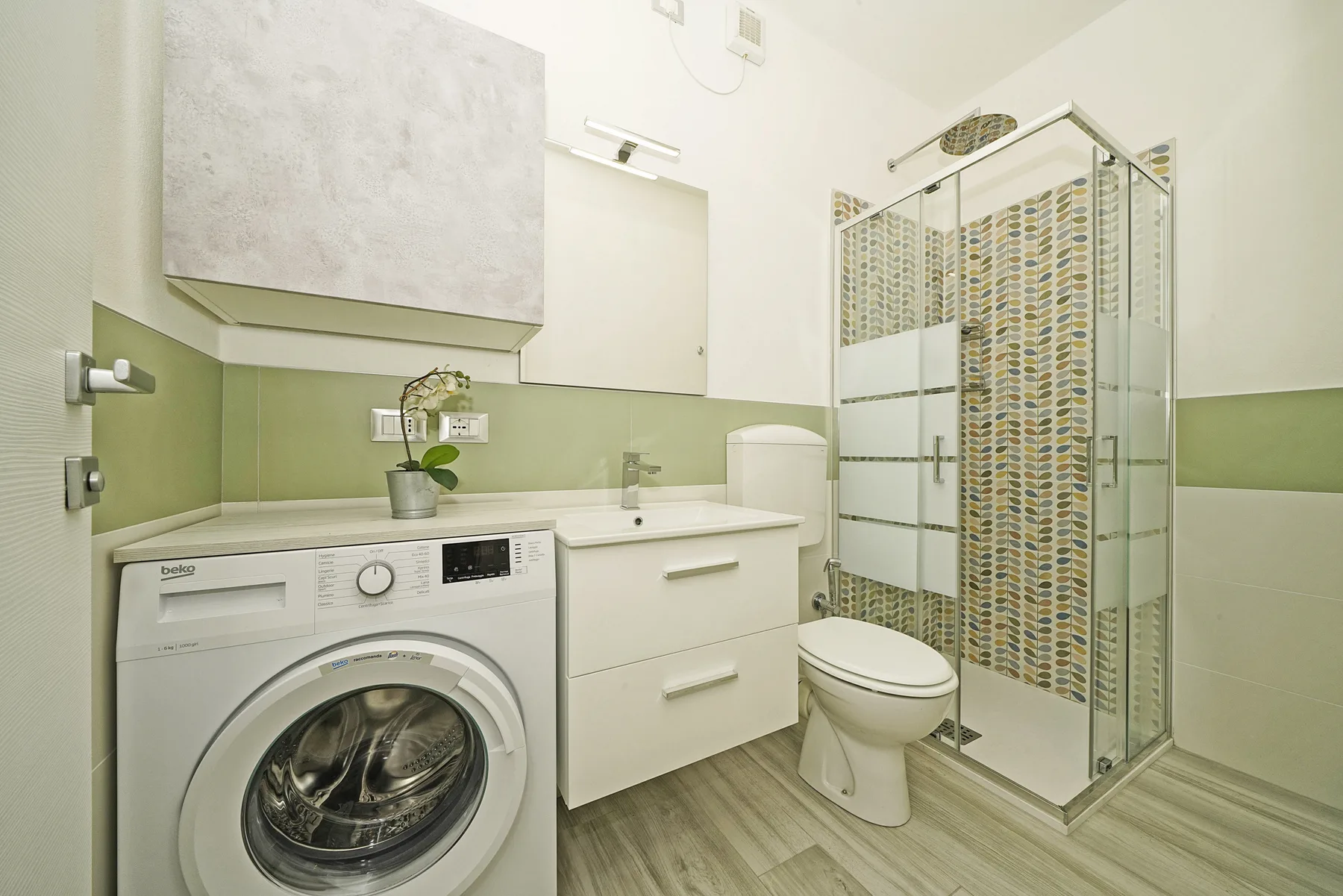 Un baño con lavadora, lavabo, inodoro y ducha de vidrio.