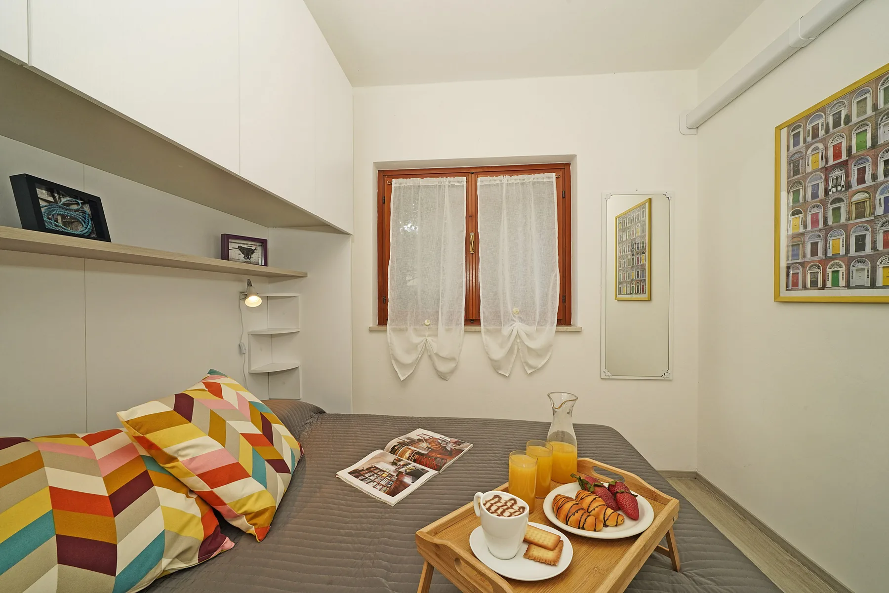 Un dormitorio con una cama, almohadas coloridas y una pequeña bandeja de desayuno.