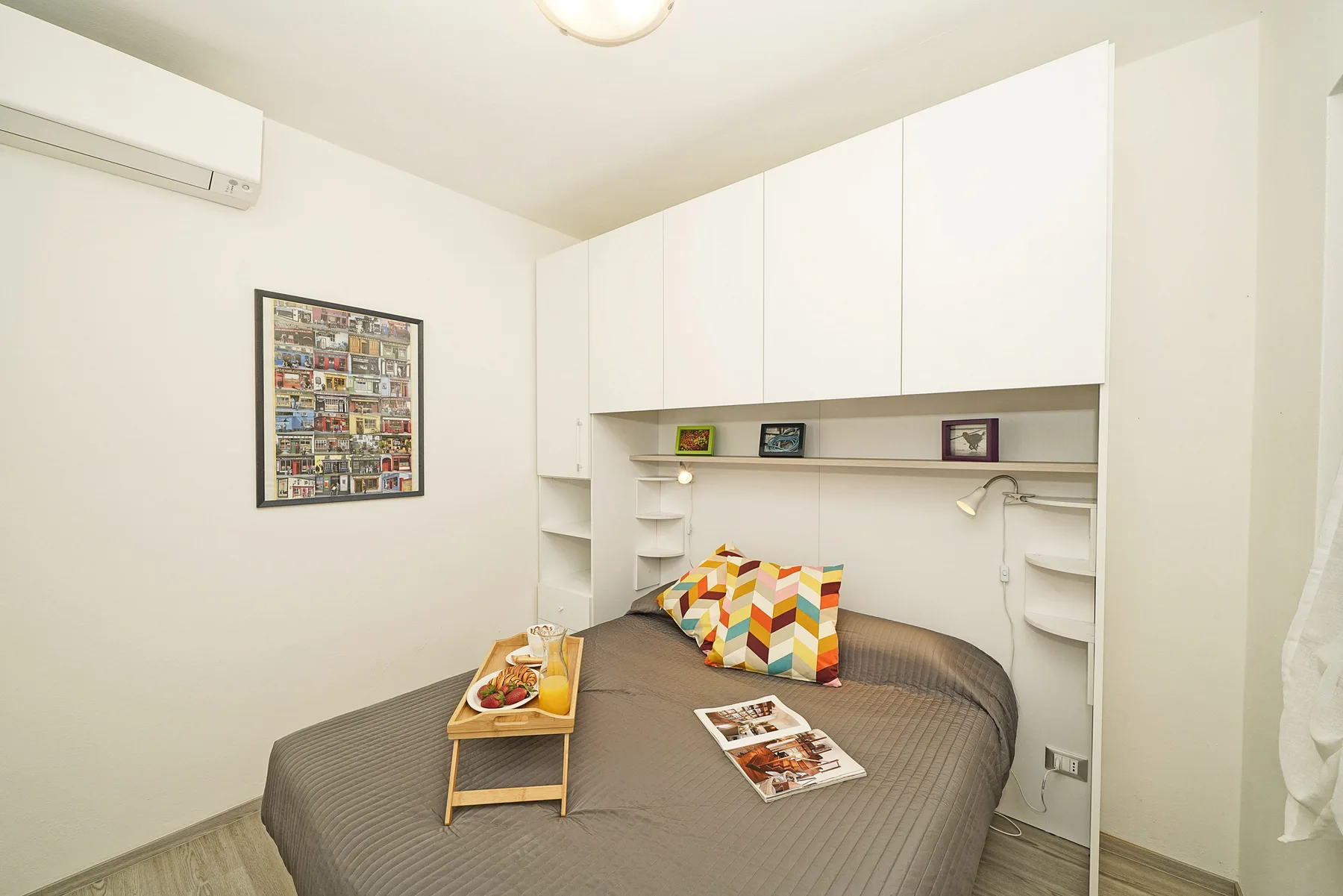 Un dormitorio con una cama bajo armarios blancos y cojines de colores.