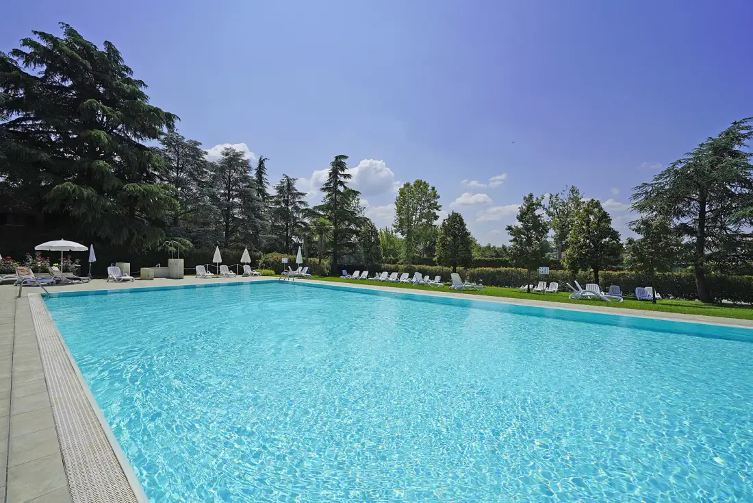 Una piscina rodeada de tumbonas y árboles bajo un cielo despejado.