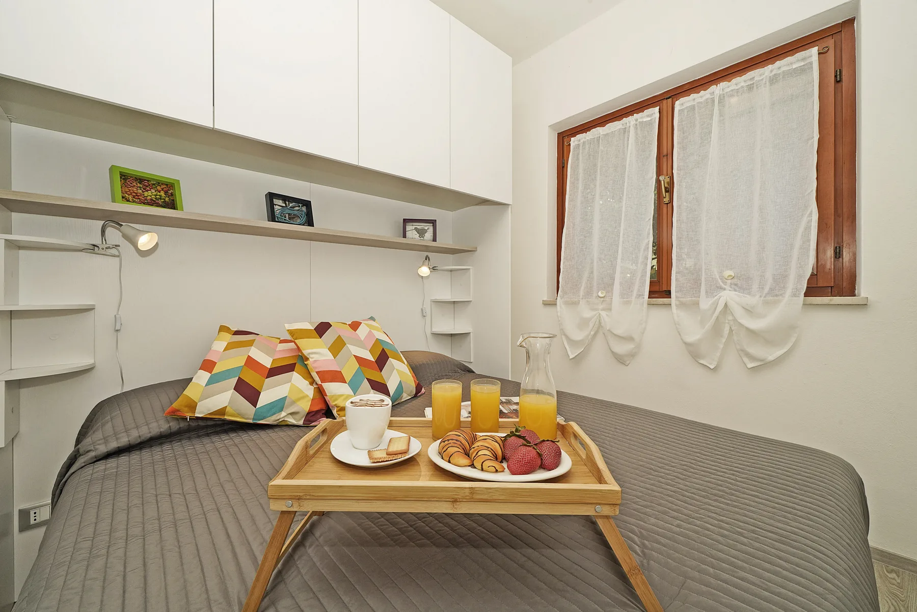Un dormitorio con una cama, cojines coloridos y una bandeja de desayuno.
