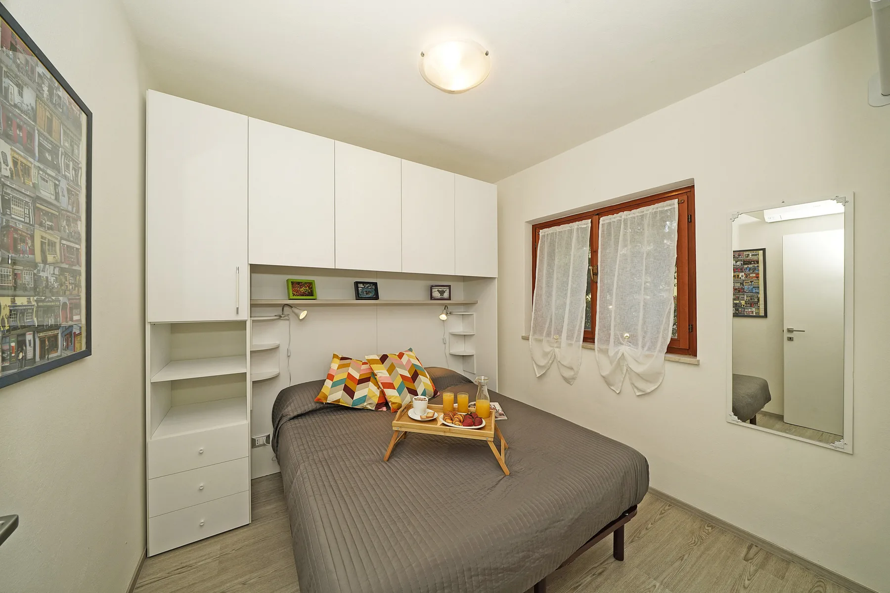 Un dormitorio con una cama doble, armarios superiores y una ventana con cortinas.