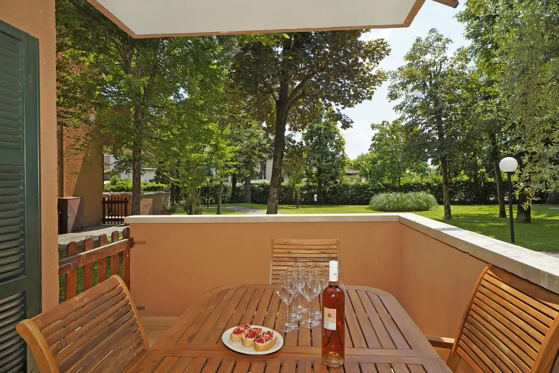 Una mesa y asientos de madera dan a un jardín verde.