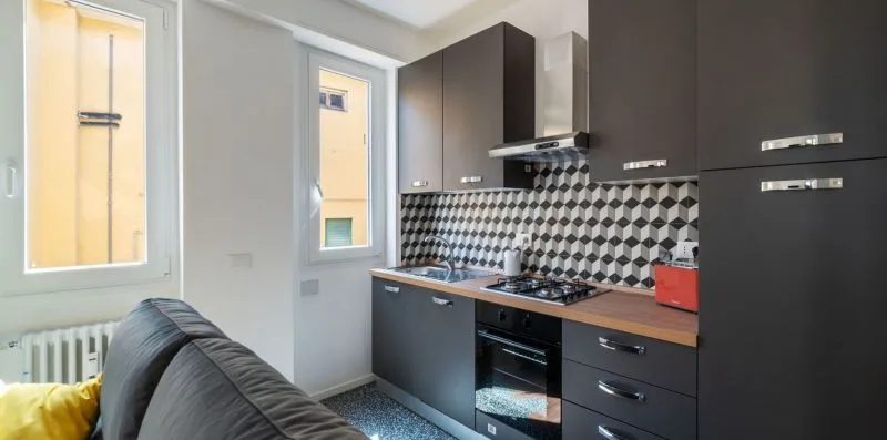Una cocina compacta con gabinetes oscuros y un salpicadero estampado junto a una zona de estar.