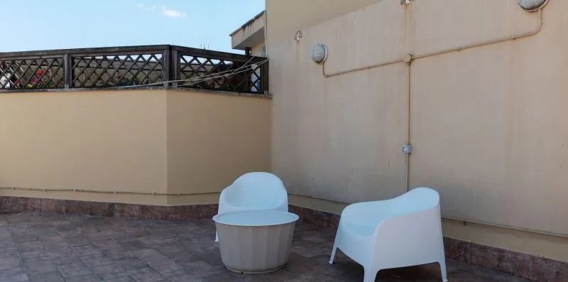Una terraza en la azotea con dos asientos blancos junto a una pared beige.