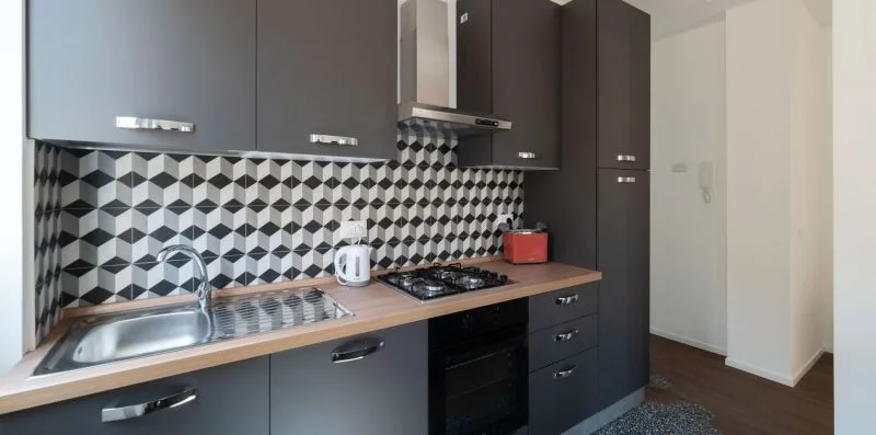 Una cocina moderna con gabinetes oscuros, salpicadero estampado y una estufa sobre la encimera.