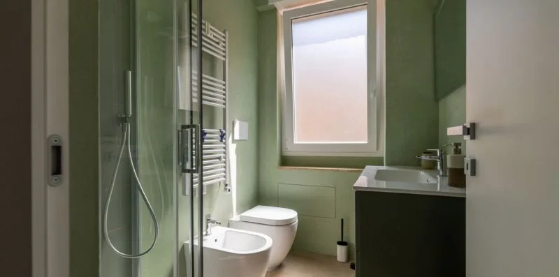 Un baño con ducha de vidrio, inodoro, lavabo y ventana esmerilada.
