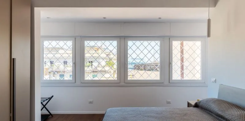 Un dormitorio con una cama y cuatro ventanas con rejas en forma de rombos.