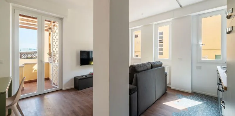 Una sala luminosa con sofá, televisor montado en la pared y ventanas amplias.