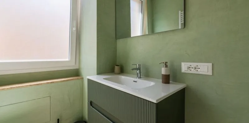 Un lavabo de baño verde con un lavamanos blanco y un espejo de pared.