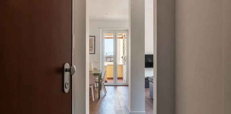 Una puerta abierta enmarca una habitación luminosa con una mesa y puertas al balcón.