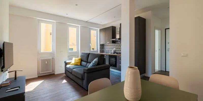 Una sala de estar con asientos oscuros, un televisor y una cocina contigua.